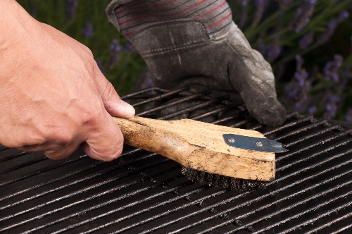 A grill owner uses a wire brush to scrub down their BBQ grill.