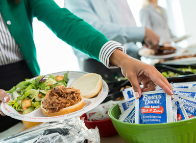 Woman in green cardigan reaching for a Famous Dave's BBQ sauce packet