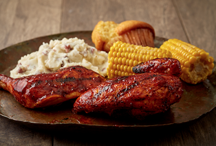 A plate of BBQ meat, corn, mashed potatoes, and cornbread muffin