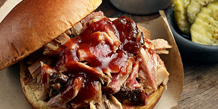 A chopped pork sandwich in a hamburger bun, smothered with BBQ sauce