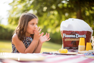 Girl licking her fingers eating Famous Dave's BBQ at a picnic.